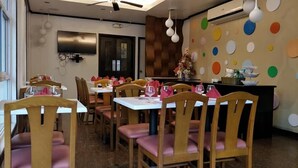 Un área de comedor con sillas y mesas de madera, un equipo de aire acondicionado instalado en la pared y una decoración mural colorida.