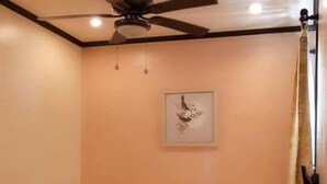 Una habitación con dos camas, un ventilador de techo, un cuadro en la pared y una ventana con cortinas.