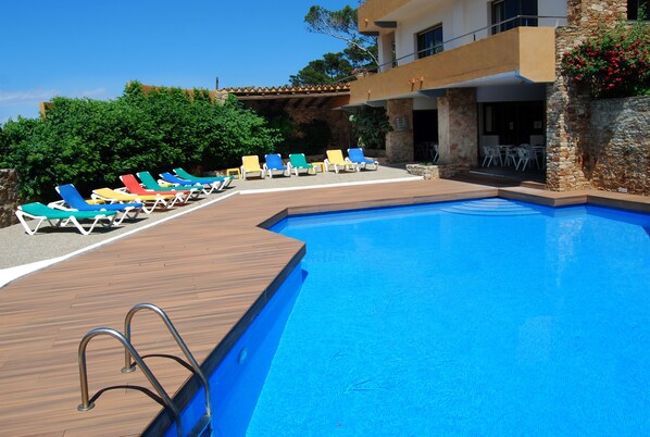 A poolside area with a wooden deck, a pool, and colorful lounge chairs.