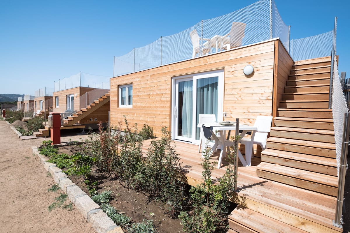 Een rij houten blokhutten met buiten trappen, een overdekt terras en een omheind tuin.