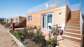 Une rangée de chalets en bois avec des escaliers extérieurs, un espace extérieur couvert aménagé en coin salon et un jardin clos.