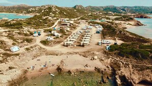 An aerial view of a coastal RV park with multiple RVs, a beach area, and a mountainous backdrop. - Camping Village Abbatoggia (La Maddalena)