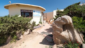 A small building with a reception area, surrounded by natural vegetation and a large rock. - Camping Village Abbatoggia (La Maddalena)