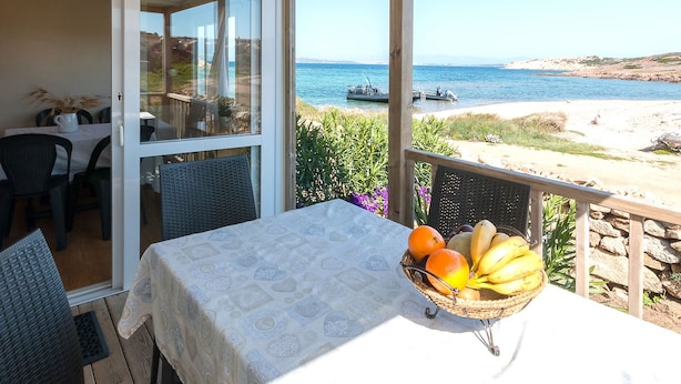 A balcony with a table set for dining, overlooking a beach and the sea. - Camping Village Abbatoggia (La Maddalena)