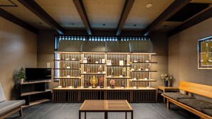 A modern interior with a wooden bench, a TV on a stand, and a wall with shelves displaying various items. - Temple Town Hotel WAQOO Horyuji (Ikaruga)