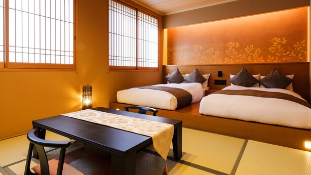A traditional Japanese-style room with tatami flooring, a low table, two beds with pillows, and a wall with a floral pattern. - Temple Town Hotel WAQOO Horyuji (Ikaruga)