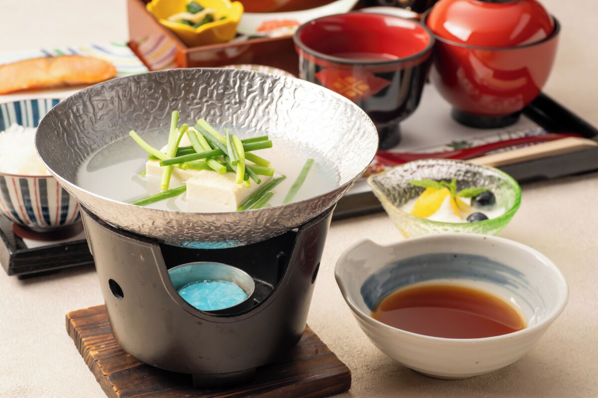 A traditional Japanese hot pot setup with tofu and green onions, accompanied by bowls of soy sauce and pickled vegetables.