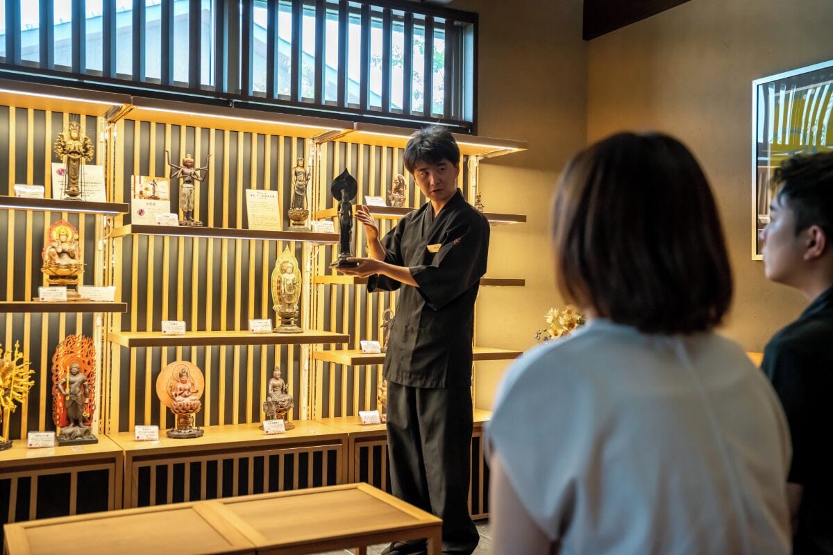 A person holding a trophy in a room with wooden shelves displaying various statues and artifacts.
