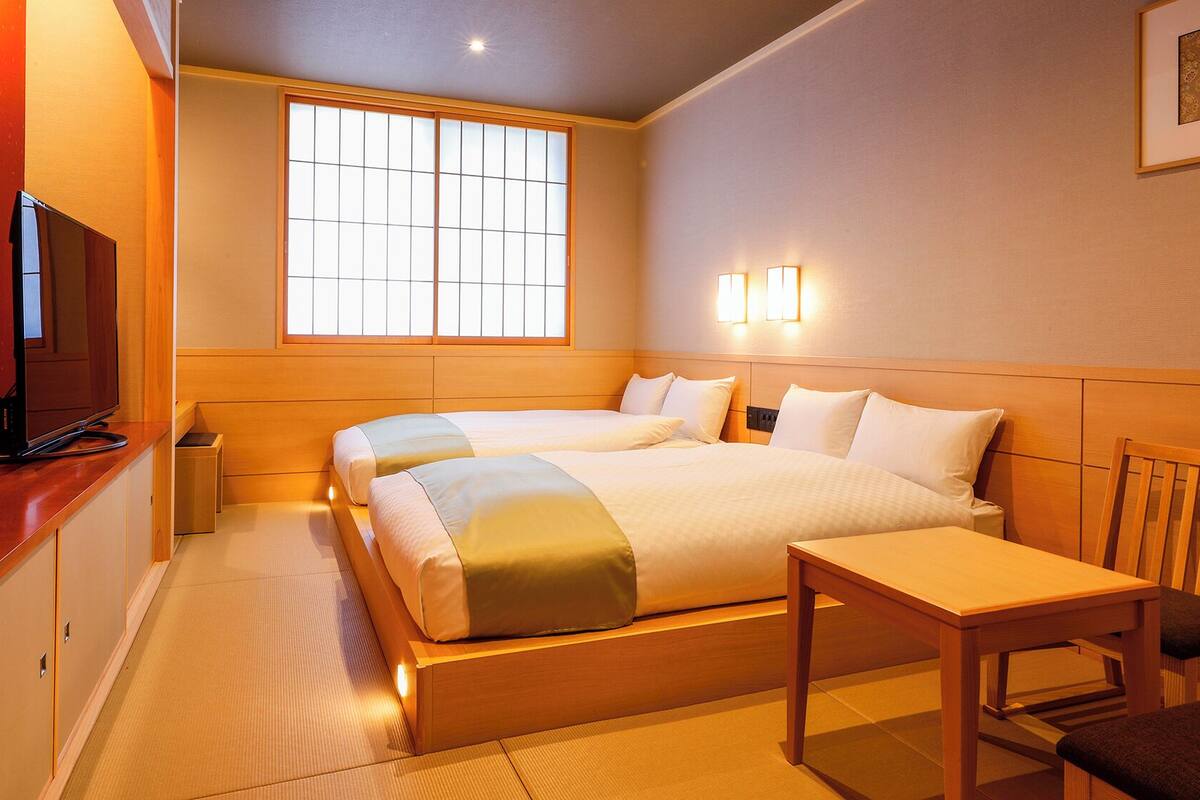 A hotel room with a bed, bedside table, chair, TV, and a window.