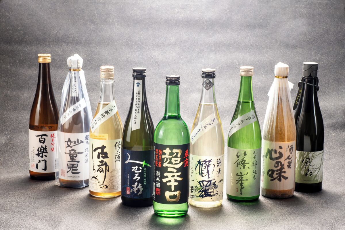 A collection of sake bottles with labels in Japanese, arranged on a textured surface.