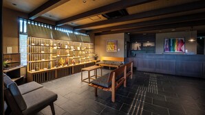 A reception area with a wooden reception desk, seating, and a wall with shelves displaying various items. - Temple Town Hotel WAQOO Horyuji (Ikaruga)