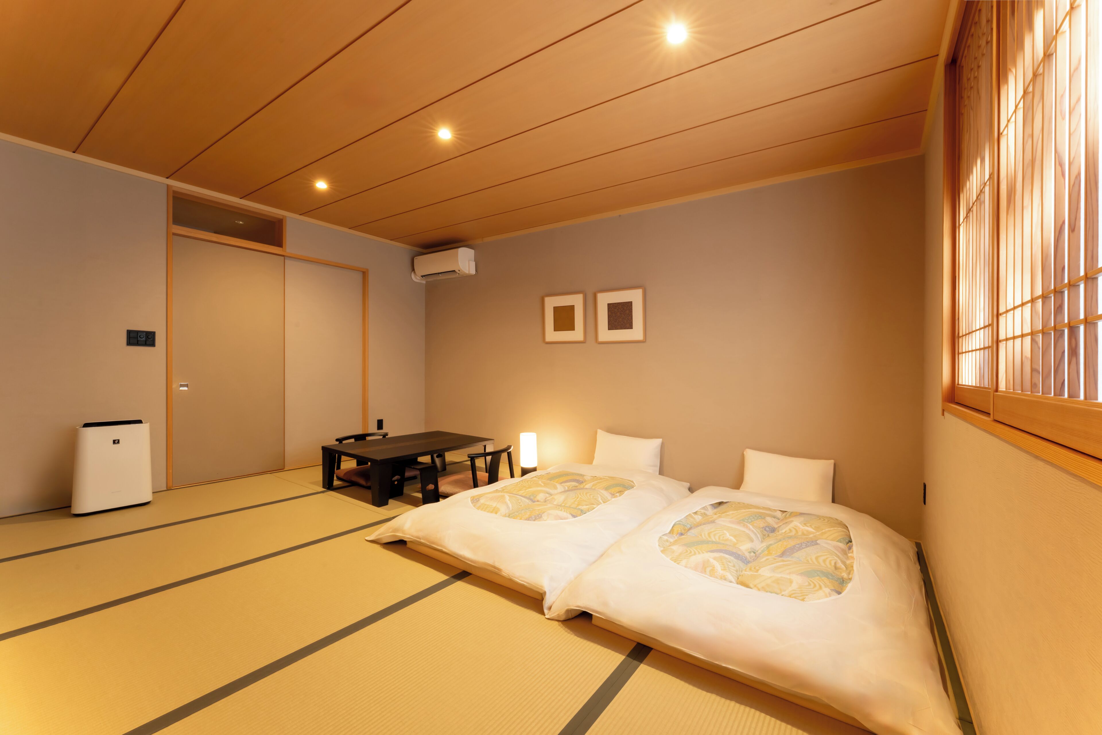 A traditional Japanese-style room with tatami flooring, a low table with chairs, a bed with white bedding, and a sliding door.