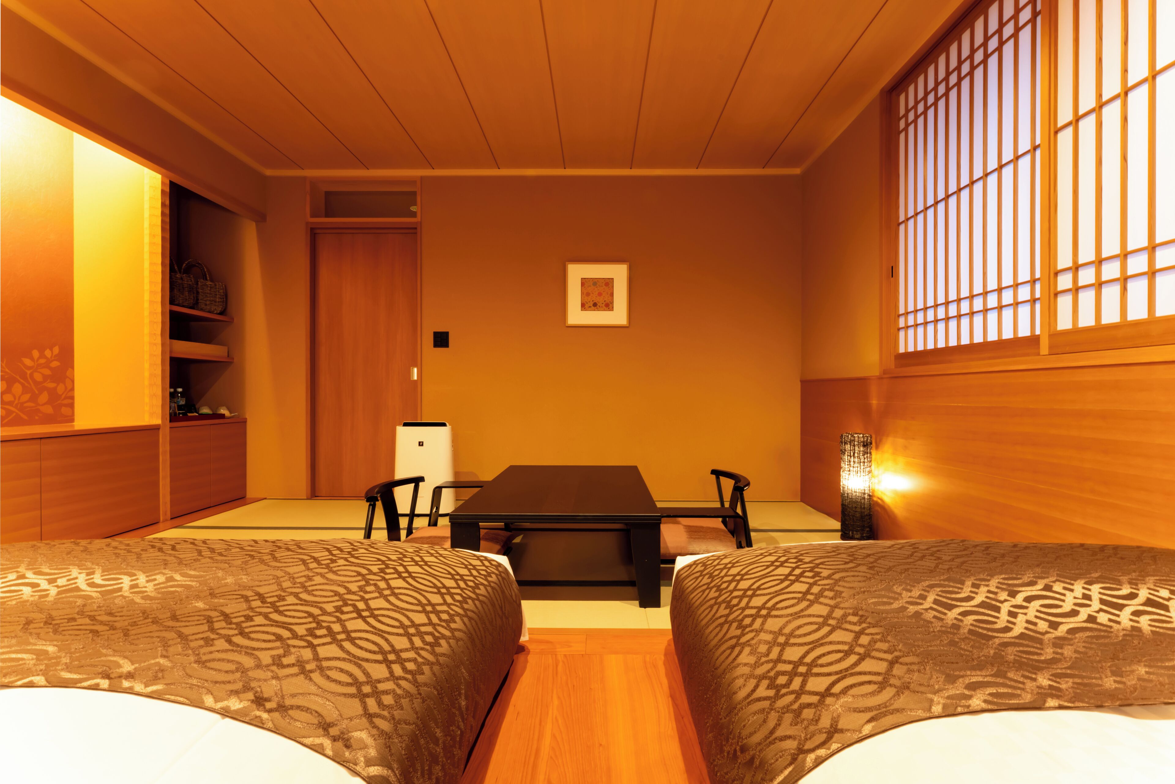 A room with two beds, a table, chairs, a small refrigerator, a cabinet, and a window with a view.
