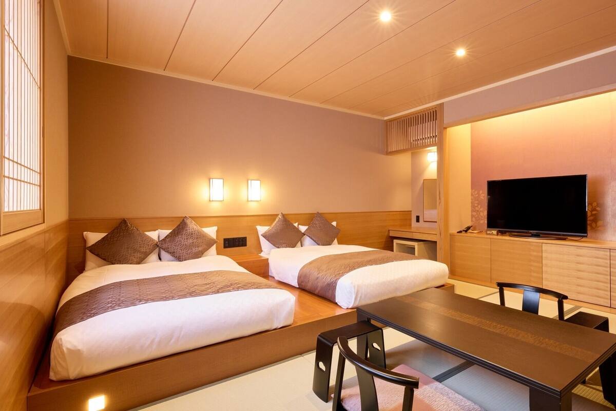 A hotel room with two beds, a TV, a desk, and a chair.