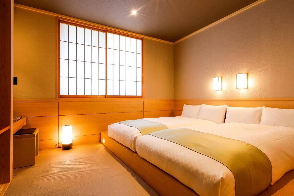 A hotel room with a large bed, a window with a view, and two wall-mounted lights.