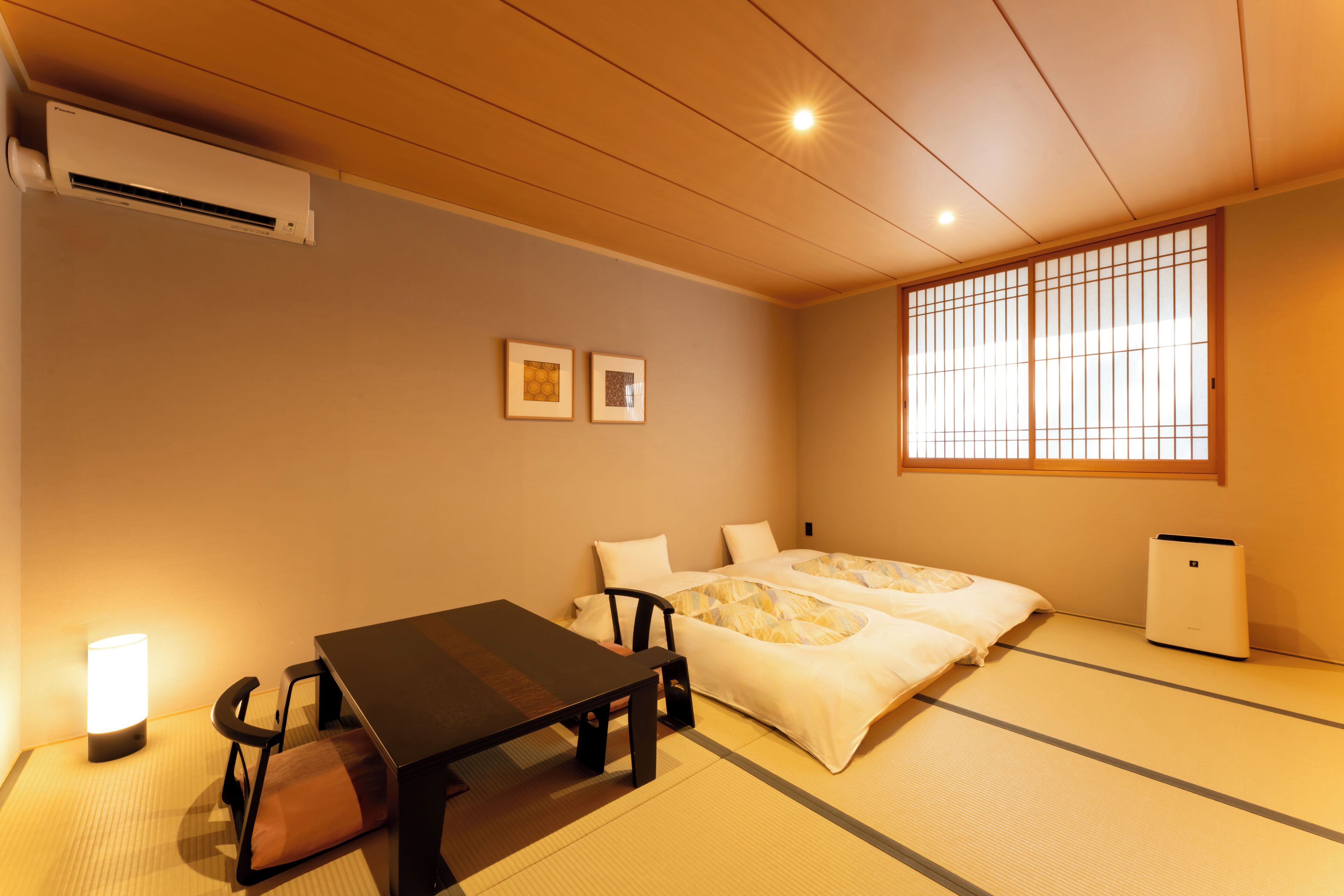 A traditional Japanese room with tatami flooring, a futon bed, a low table with a chair, and a small air conditioning unit.