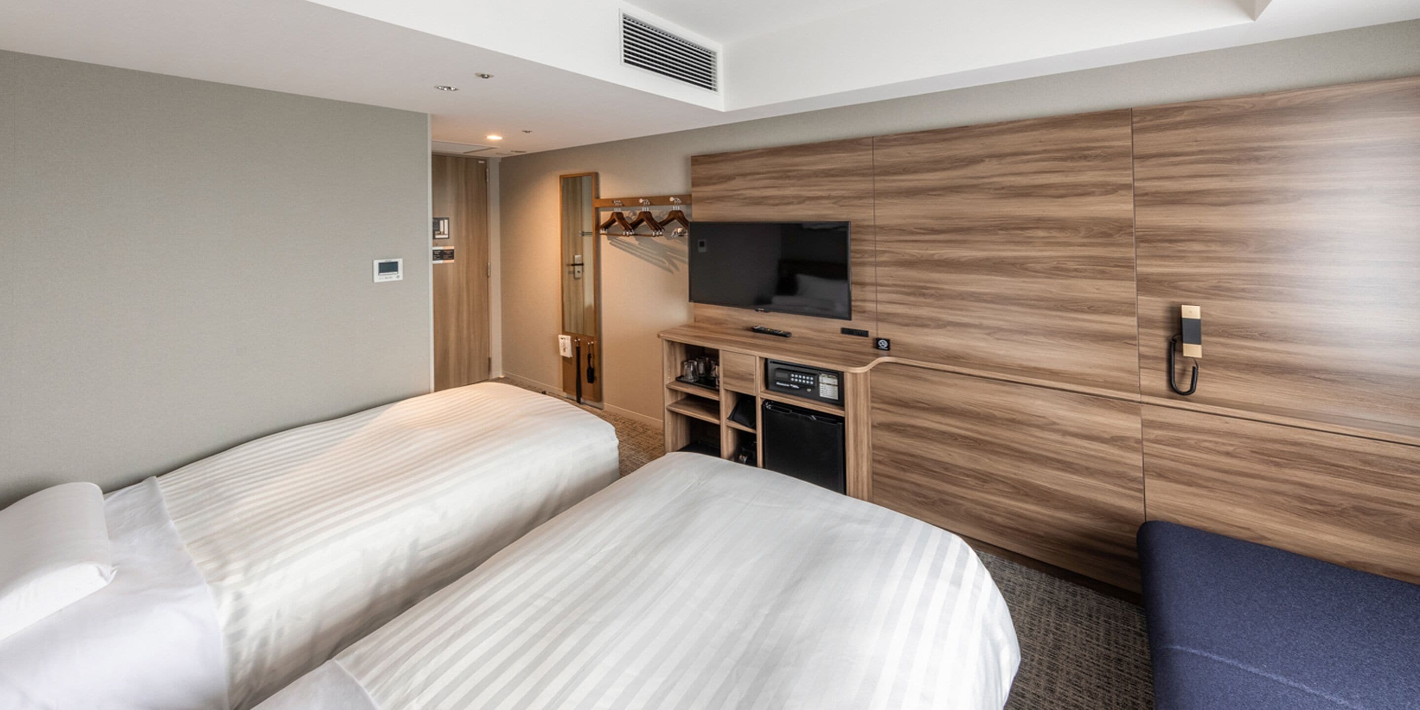 Ein Hotelzimmer mit zwei Betten, einem Fernseher, einer Minibar und einem Holzschrank.