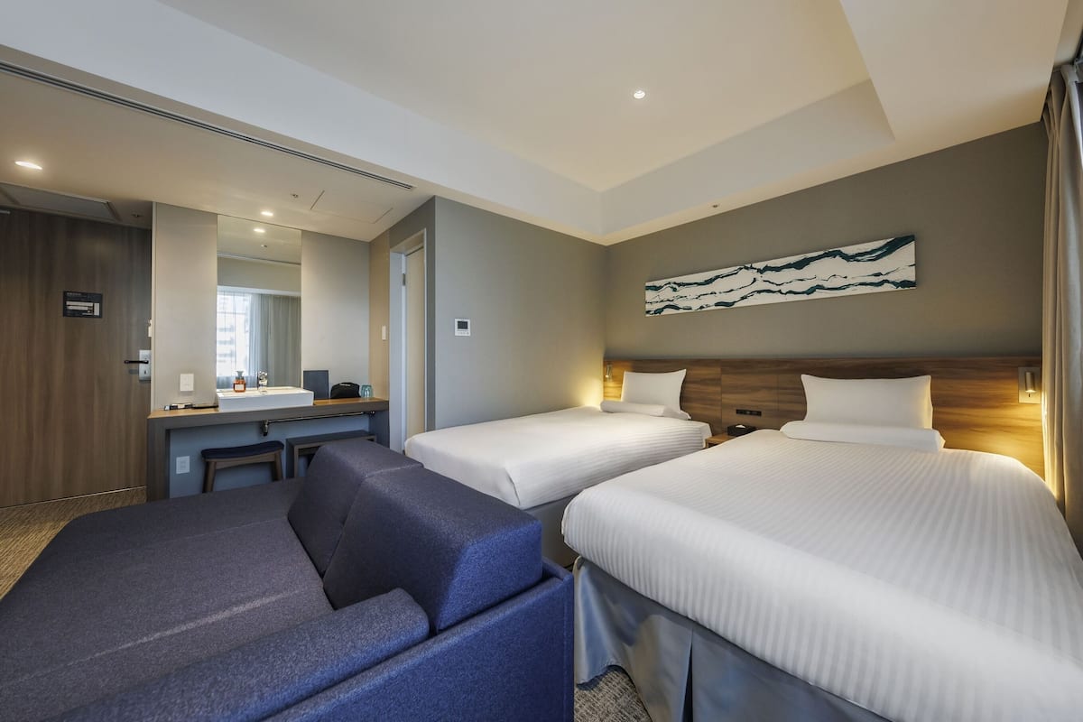 A hotel room with two beds, a desk with a mirror, and a large artwork on the wall.