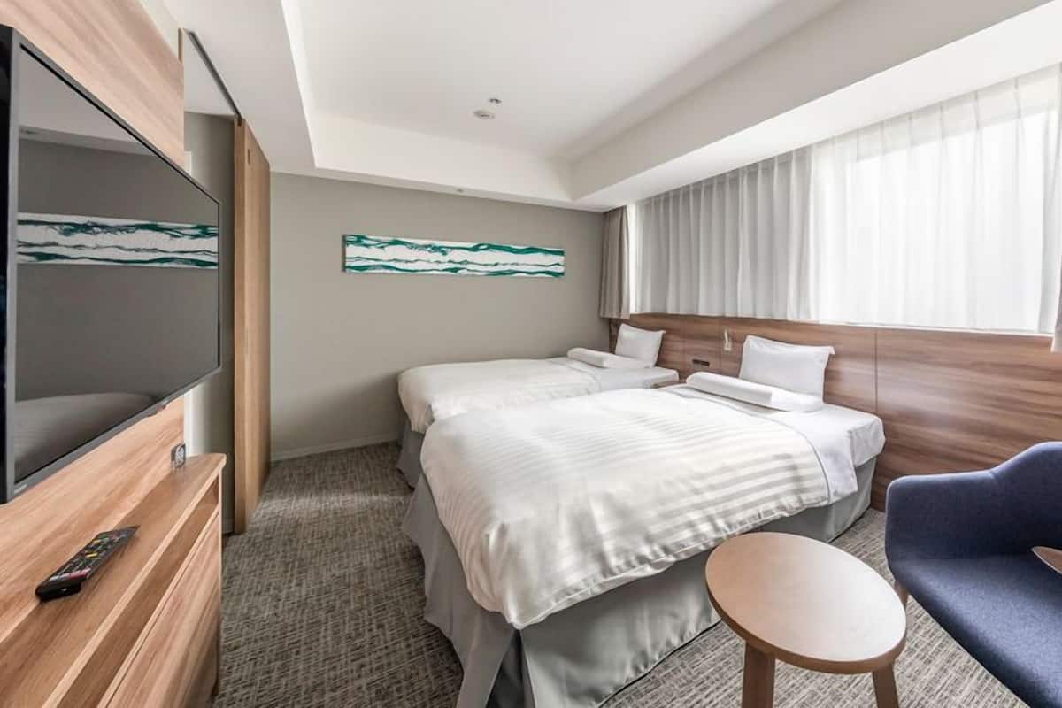 A hotel room with a bed, a TV, a chair, a small table, and a painting on the wall.