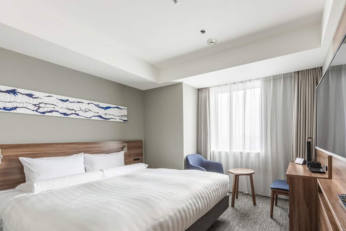 A hotel room with a large bed, a desk with a chair, a television, and a window with curtains.