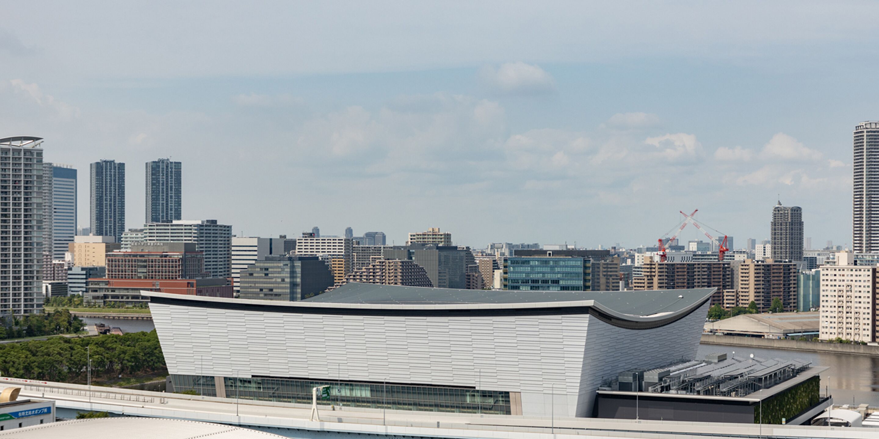 Un edificio moderno con techo curvo, rodeado de edificios altos y un río.