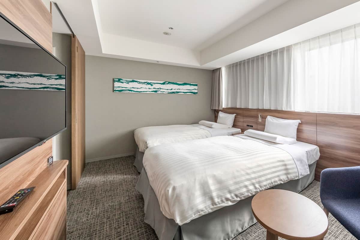 A hotel room with a bed, a TV, a chair, and a window with curtains.