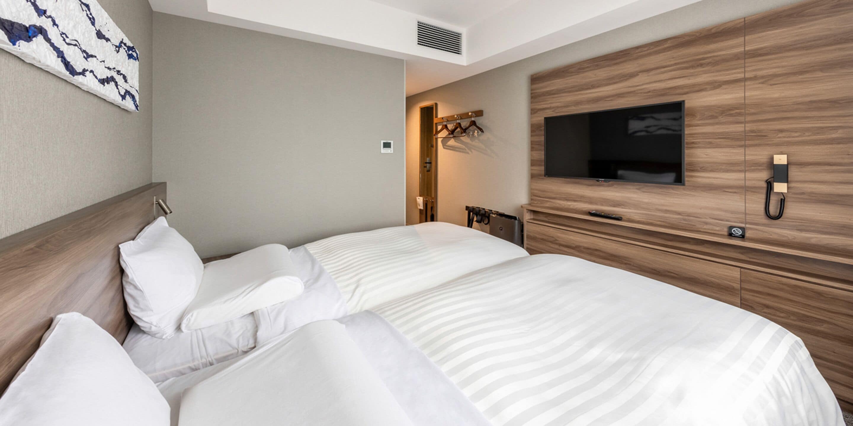 Een moderne hotelkamer met een groot bed, een flatscreen televisie aan een houten muur, een kapstok en een klein bureau met een stoel.