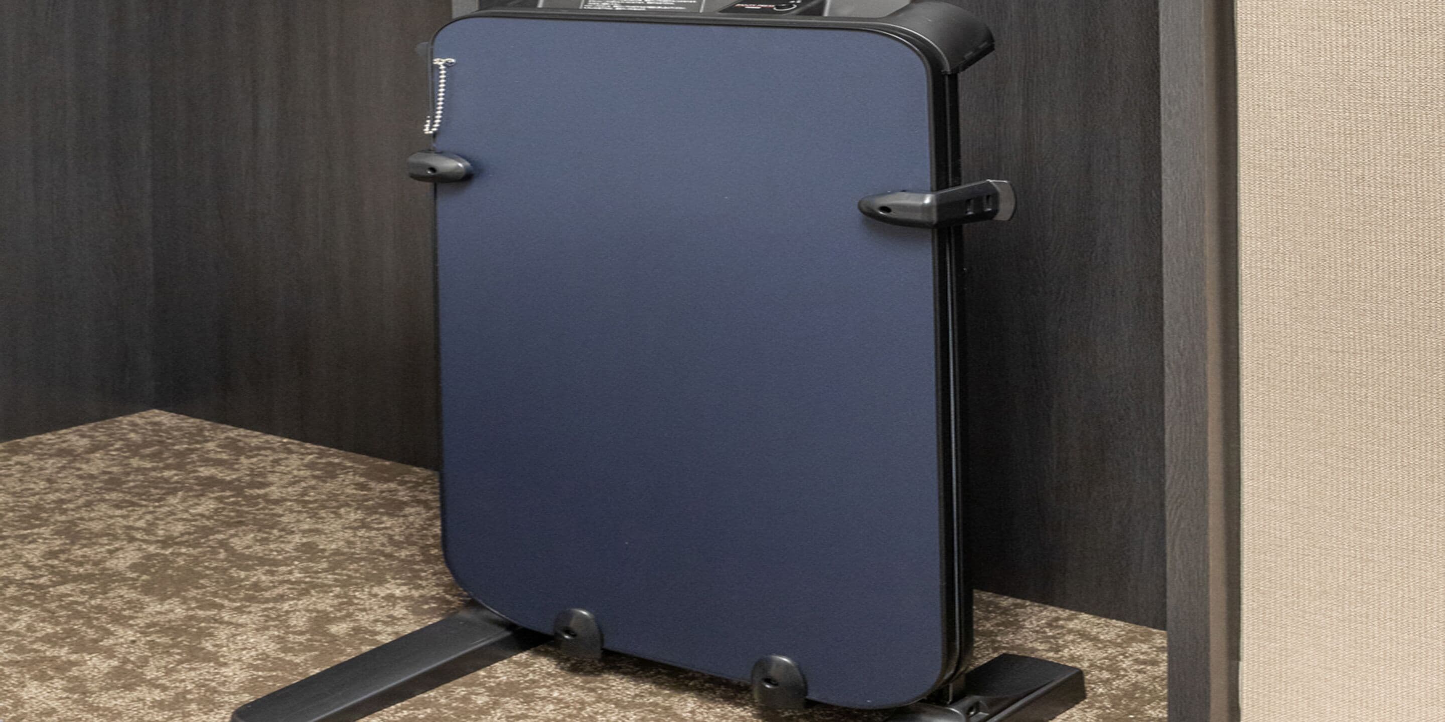 A blue suitcase on a stand in a room with a textured floor and dark walls.