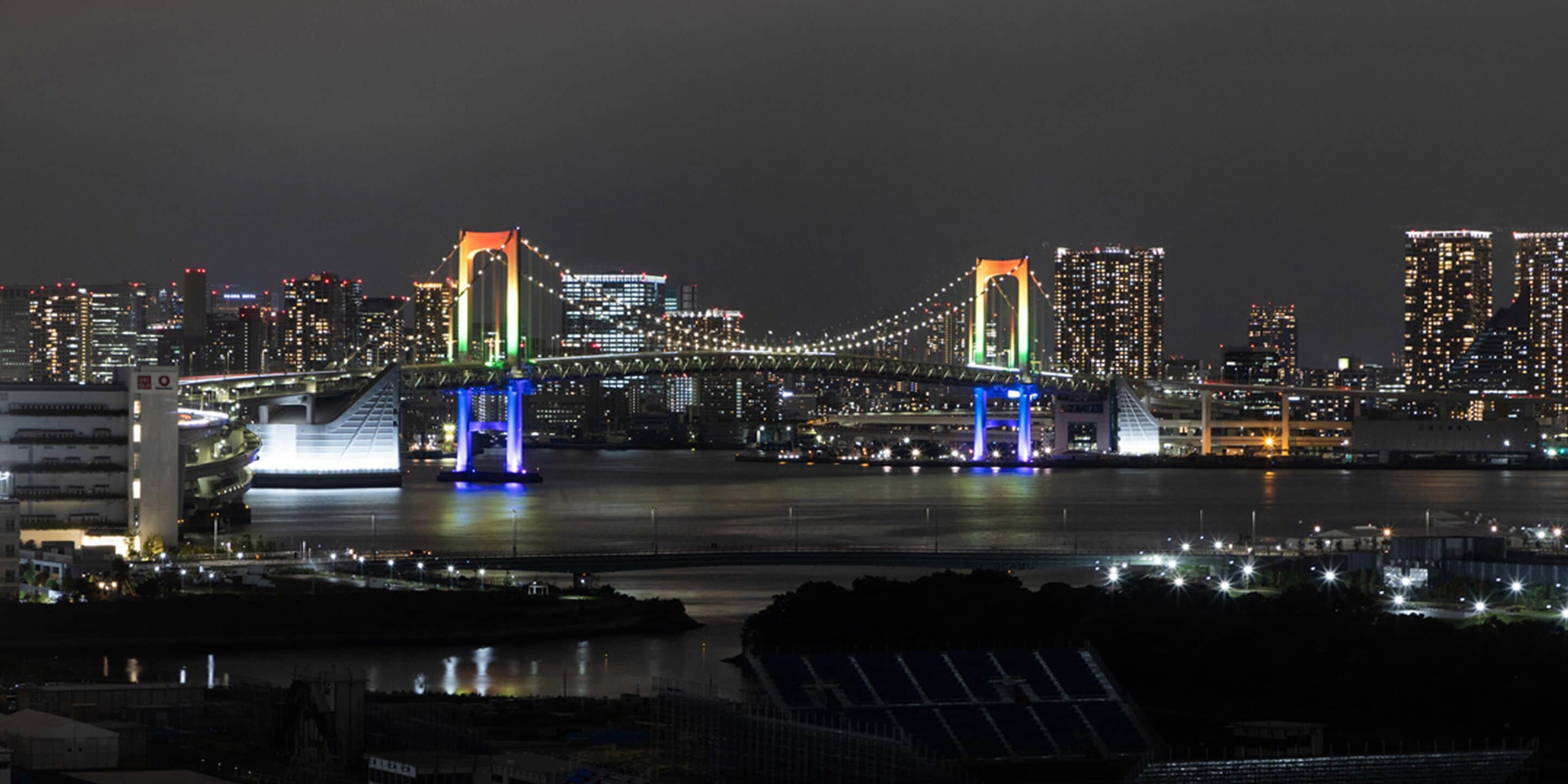 A nighttime cityscape with a prominent illuminated bridge spanning a river.