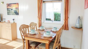 A dining area with a wooden table set for four, a window with curtains, a painting on the wall, and a small shelf with a lantern. - 2 bedroom nice home in Tzummarum (Tzummarum)