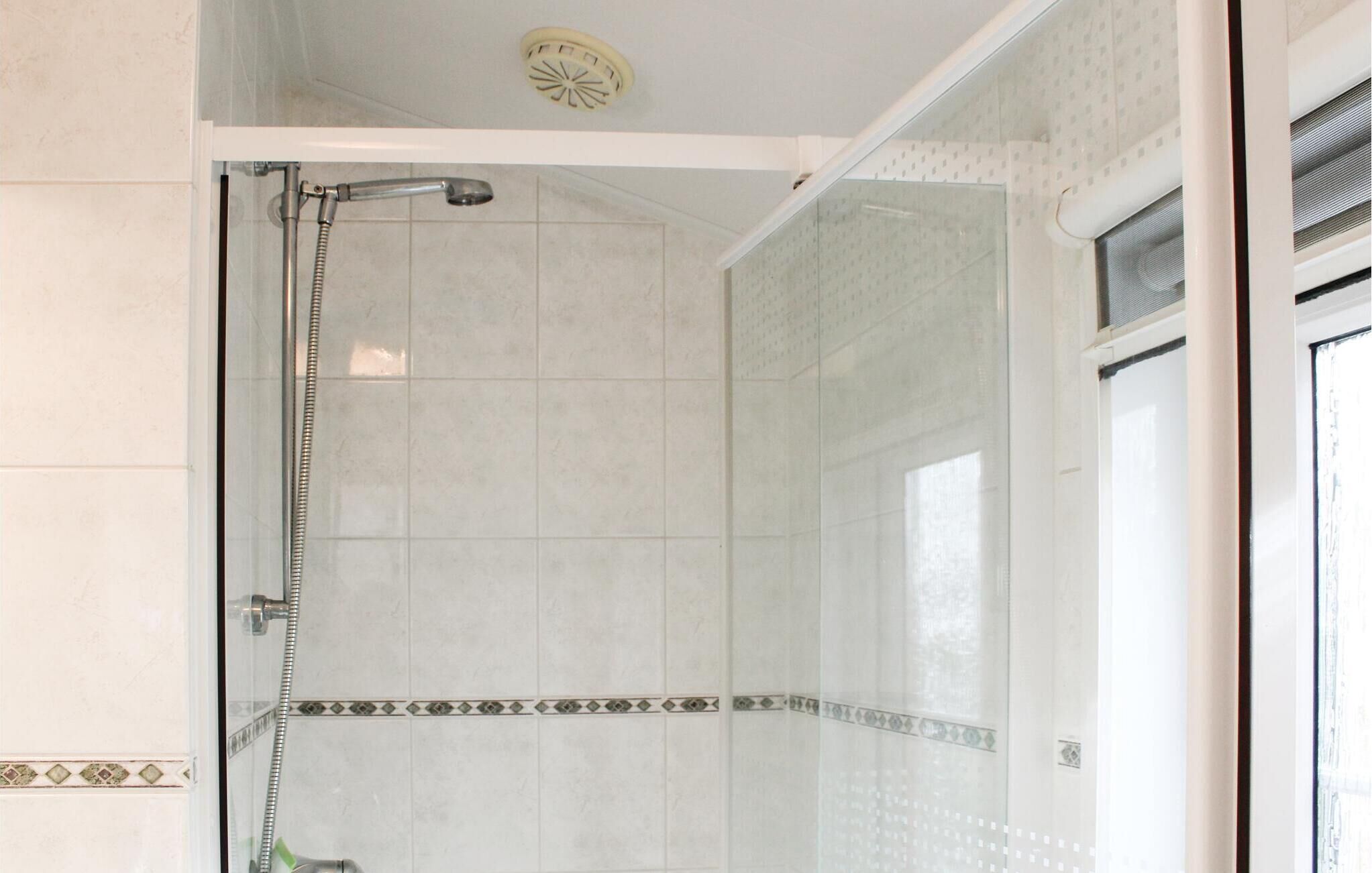 A shower with a glass door, tiled walls, and a patterned border.