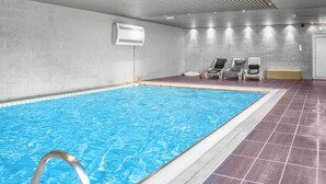 An indoor swimming pool with a clear water surface, a pool ladder, and a tiled floor. There are lounge chairs and a white air conditioning unit on the wall. - Stunning apartment in Vossestrand (Vossestrand)