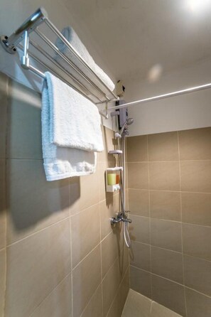 A bathroom with beige tiles, a towel rack with two white towels, a showerhead, and a soap dispenser.