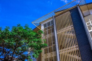 Un bâtiment à l’architecture moderne, caractérisé par une structure verticale imposante, agrémentée d’une série de lignes horizontales et doté d’un balcon avec une rambarde en métal.
