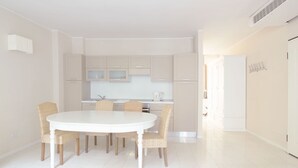Uma cozinha moderna com armários brancos, uma mesa de jantar branca e cadeiras de vime.