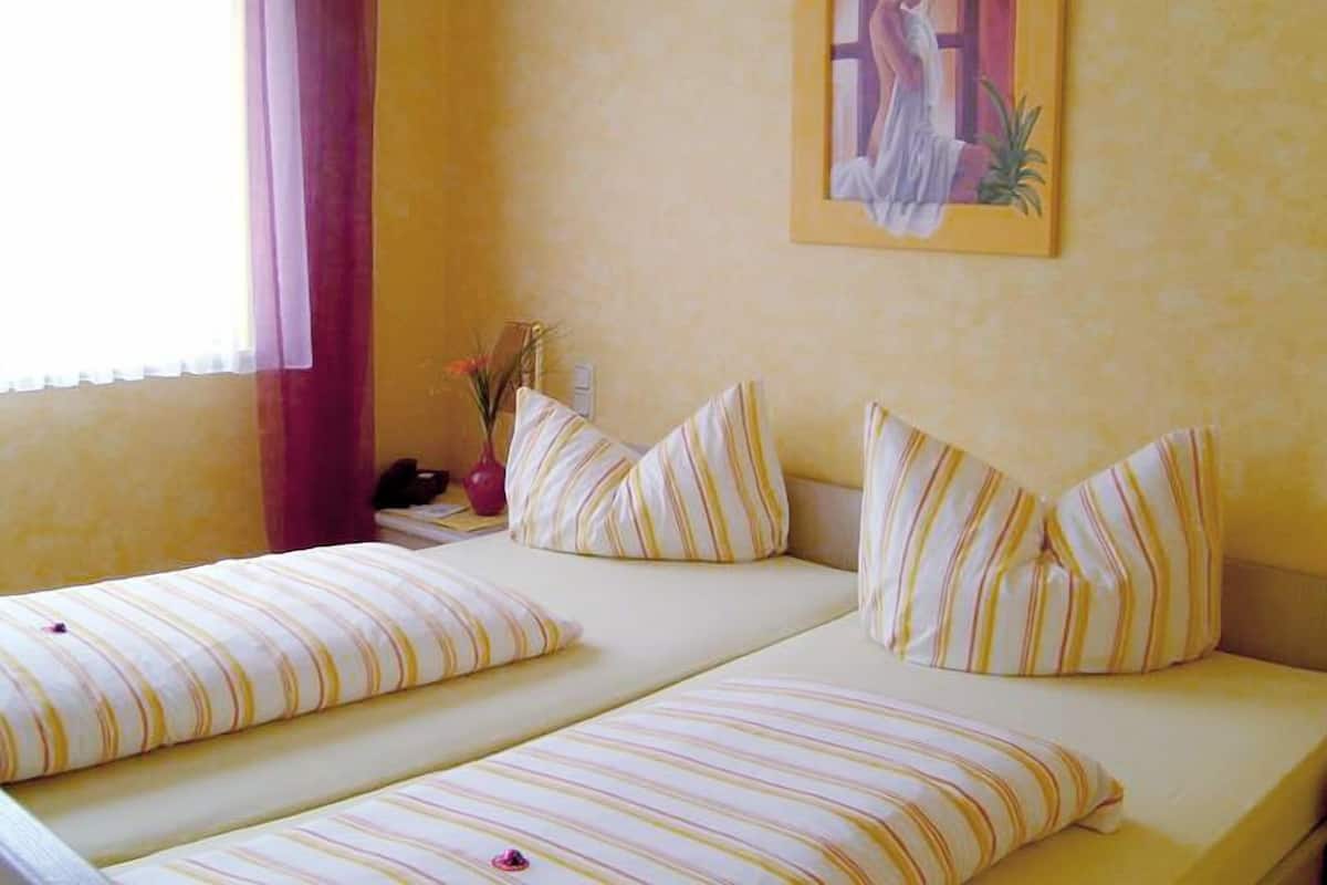 A room with two beds, each with striped bedding, a painting on the wall, and a window with curtains.