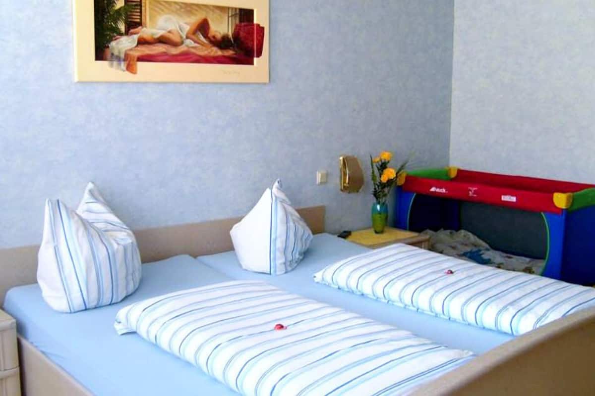 A bedroom with two beds, striped pillows, a framed picture on the wall, and a small table with a vase of flowers.