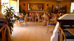 A restaurant with wooden chairs and tables, a tiled floor, and a large mirror on the wall. - Stadt Cafe Pension Grünstadt (Gruenstadt)