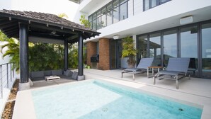 Ein moderner Poolbereich im Freien mit Liegestühlen, einer Pergola und Blick auf ein Hochhaus.