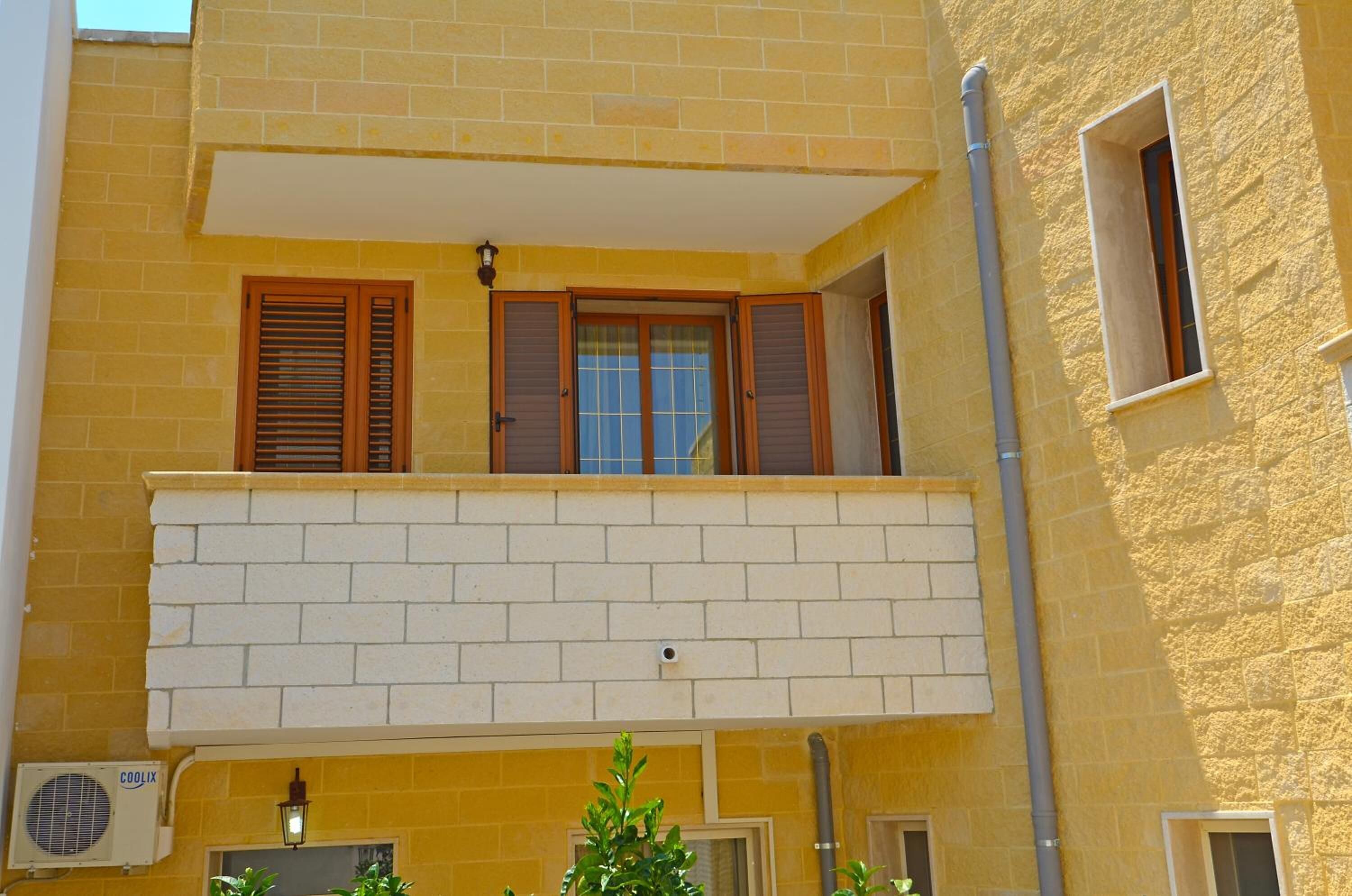 Ein gelbes Gebäude mit Balkon, einem Fenster mit Rollläden und einer Klimaanlage.