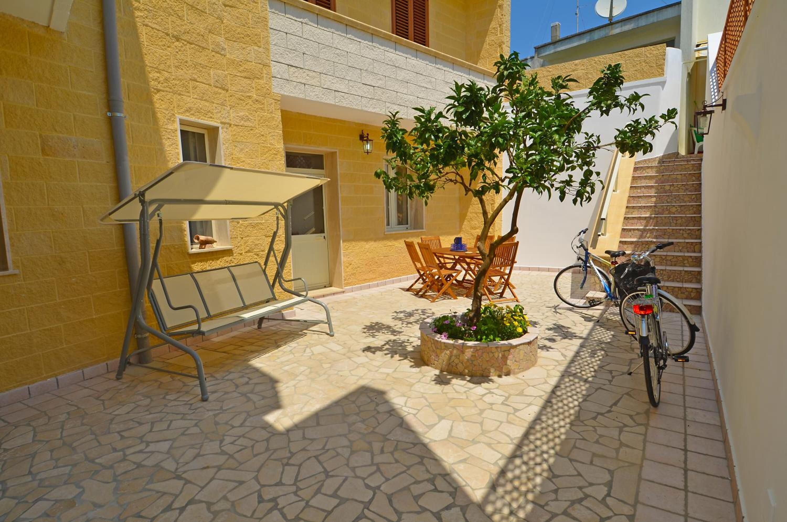 Ein Innenhof mit Schaukel, Tisch mit Stühlen, einem Blumentopf und einem Fahrrad.