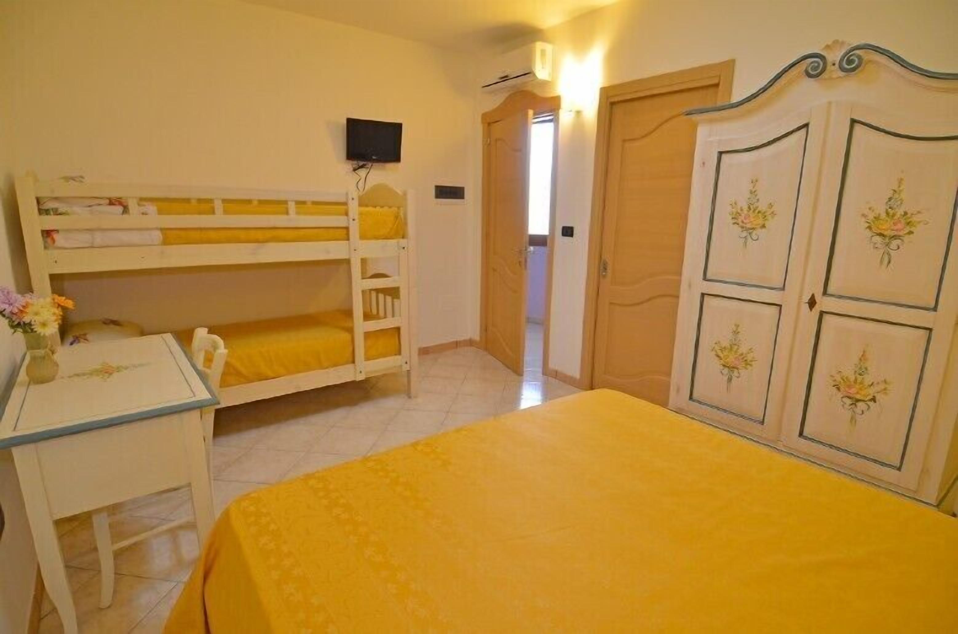 Une chambre avec des lits superposés, un bureau, une chaise et un lit recouvert d’une couverture jaune.