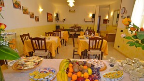 Un comedor con varias mesas dispuestas para una comida, con una variedad de frutas y pasteles.