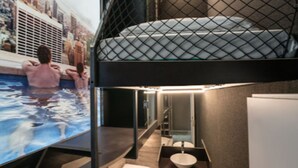 A modern hotel room with a bunk bed, a large window overlooking a cityscape, a private pool area, and a minimalist bathroom. - BoxHotel Hannover (Hannover)