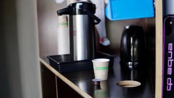 Una cafetera, un vaso desechable y un recipiente pequeño sobre una encimera.