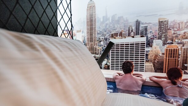A couple relaxing in a rooftop infinity pool with a cityscape view, including a prominent skyscraper. - BoxHotel Hannover (Hannover)