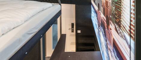 A narrow room with a bunk bed and a mural of a cityscape.