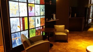 A hotel lobby with a glass wall displaying colorful graffiti art, a seating area with two chairs and a small table, and a reception desk with a sign reading "BOX HOTEL". - BoxHotel Hannover (Hannover)