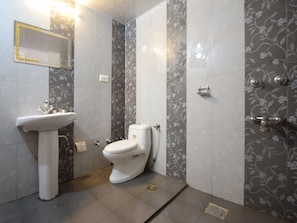 Un baño con lavamanos, inodoro y zona de ducha blancos.
