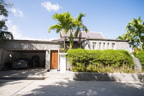 A stone building with a garage, palm trees, and a well-maintained garden.